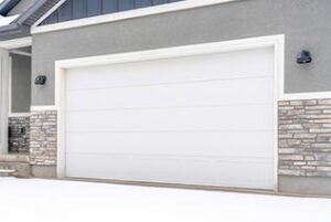 Wide white garage door of home with gray exterior wall on a snowy winter day